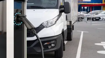 Ein weißer Transporter lädt an einer E-Ladesäule auf einem Unternehmensparkplatz